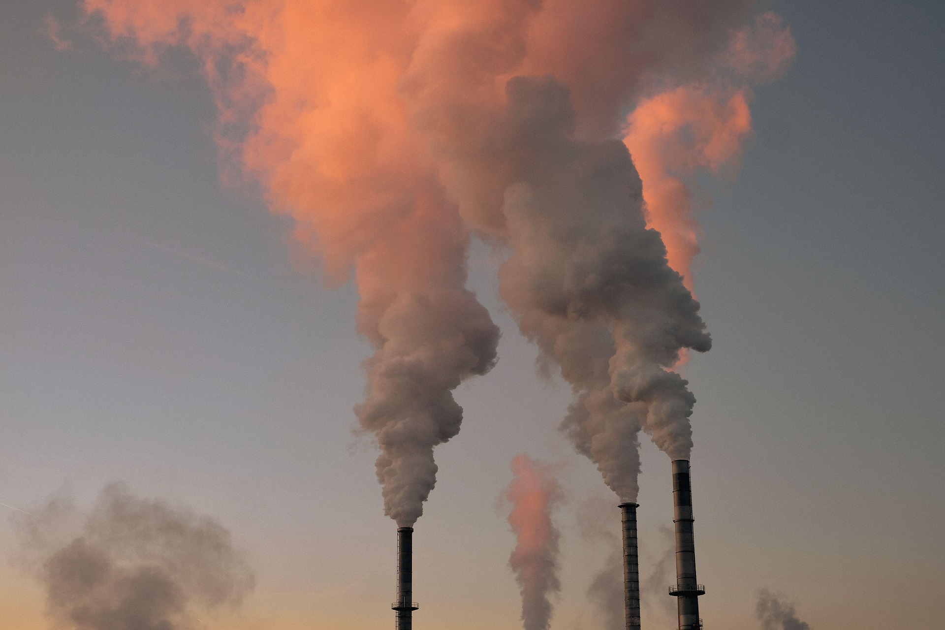 Industrieanlage mit rauchenden Schornsteinen im Abendlicht